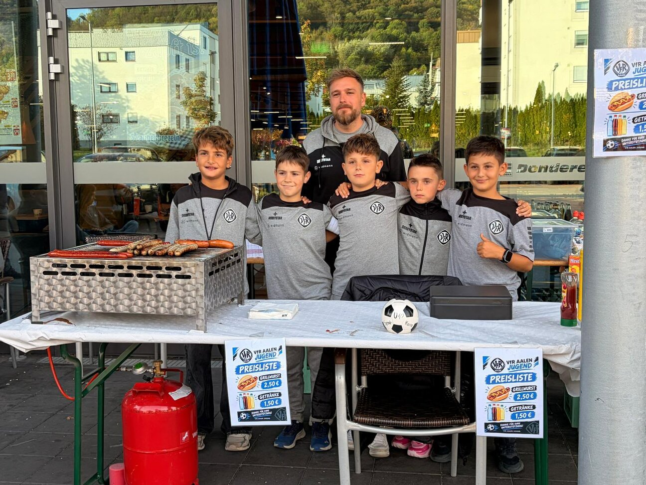 VfR-Jugendspieler und ein Betreuer am Grillstand vor EDEKA Donderer.